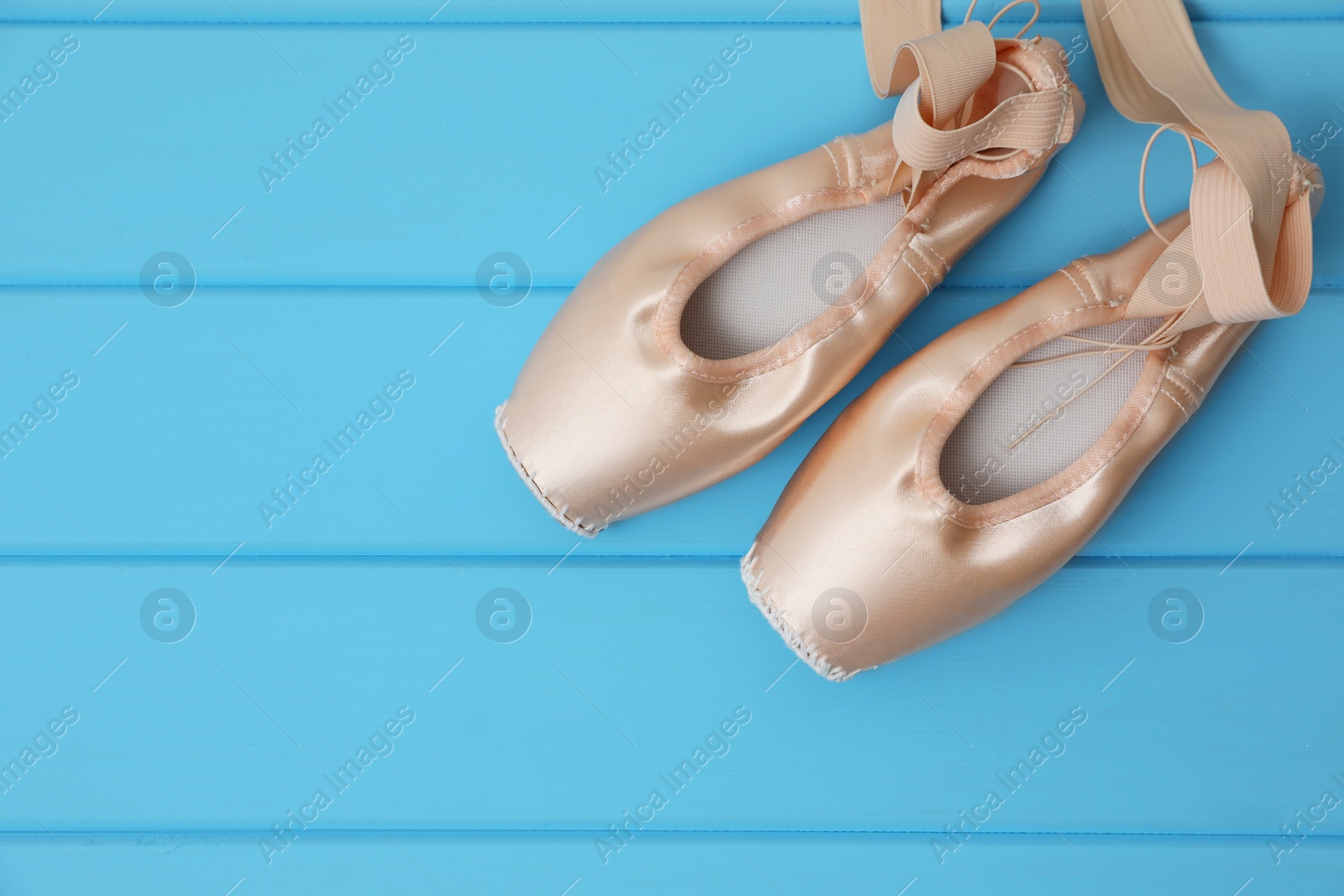Photo of Beautiful beige ballet shoes with cute ribbons on light blue wooden table, top view. Space for text