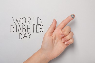 Woman showing finger with drawn blue circle near text World Diabetes Day on light background, closeup