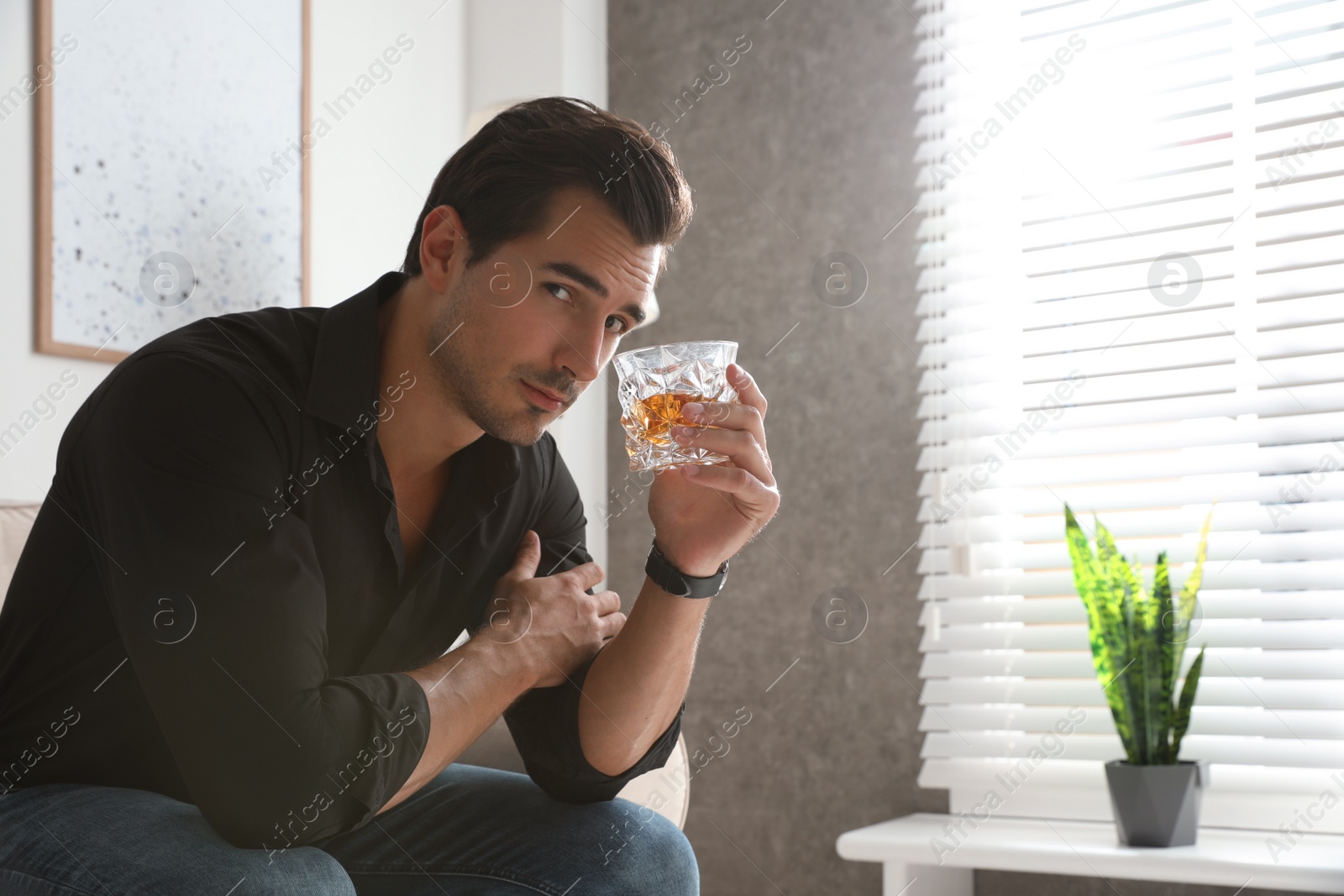 Photo of Young man with glass of whiskey at home. Space for text