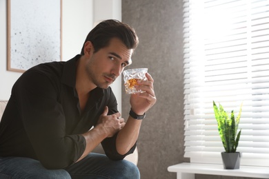 Young man with glass of whiskey at home. Space for text