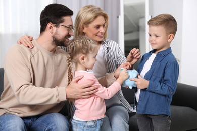 Photo of Family budget. Children and their parents putting coins into piggy bank indoors