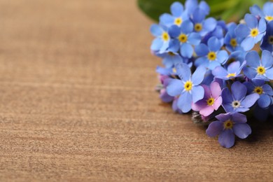 Photo of Beautiful blue Forget-me-not flowers on wooden table, closeup. Space for text