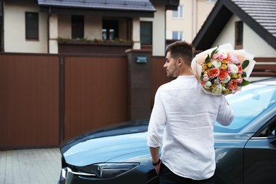 Young handsome man with beautiful flower bouquet near car outdoors, space for text