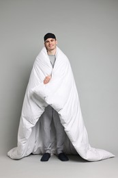 Photo of Man in pyjama and sleep mask wrapped in blanket on grey background