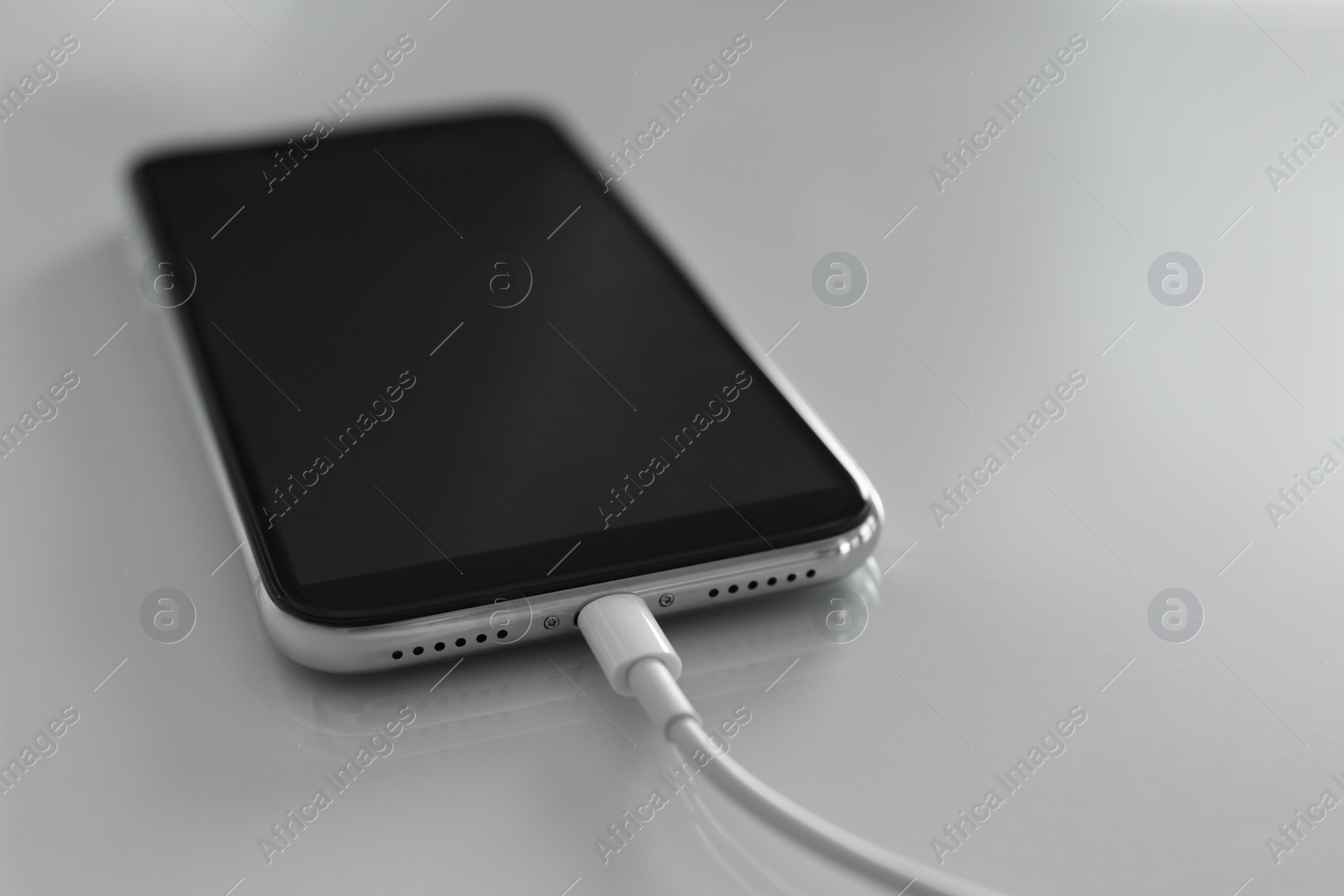 Photo of Mobile phone charging on white table, closeup
