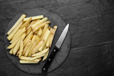 Cut raw potatoes with knife on black table, top view. Space for text