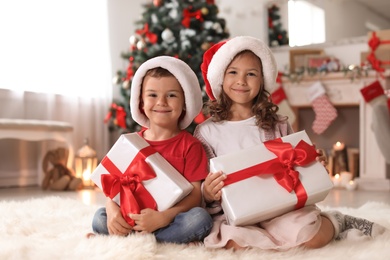 Cute little children in Santa hats with Christmas gift boxes at home