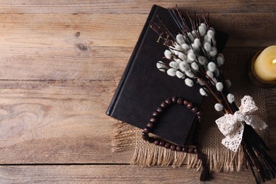 Rosary beads, Bible, burning candle and willow branches on wooden table, flat lay. Space for text