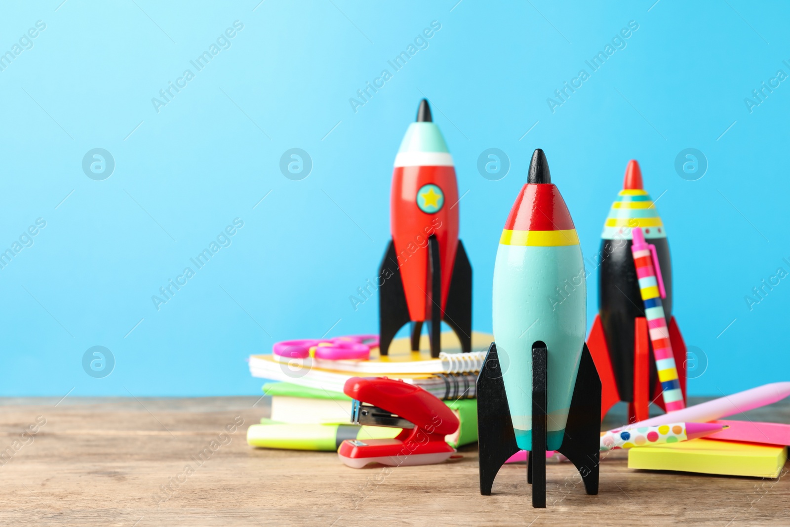 Photo of Bright toy rockets and school supplies on wooden table. Space for text