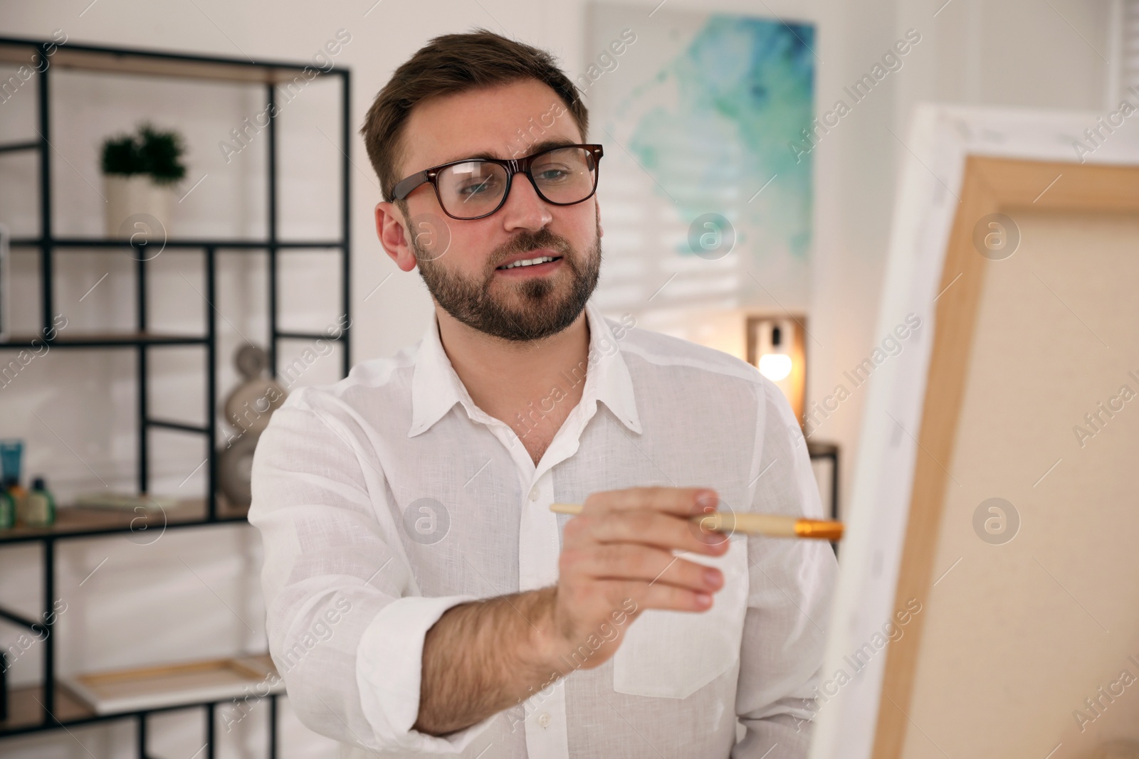 Photo of Young man painting on easel with brush in artist studio