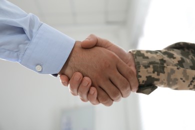 Soldier and businessman shaking hands indoors, closeup