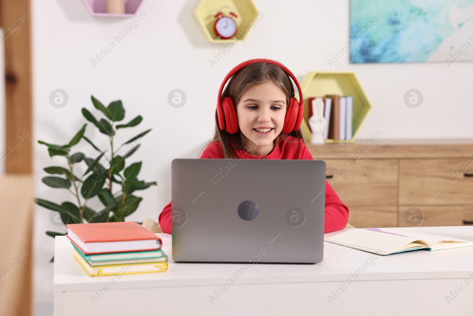 Photo of E-learning. Cute girl using laptop and headphones during online lesson at table indoors