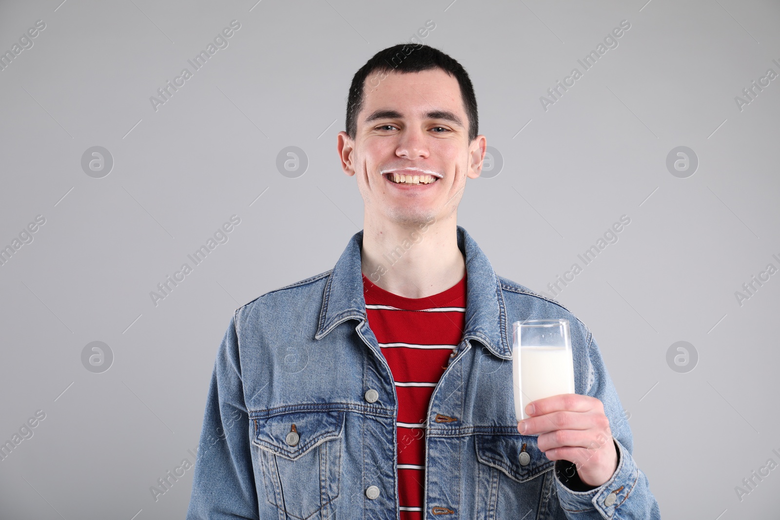 Photo of Happy man with milk mustache holding glass of tasty dairy drink on gray background