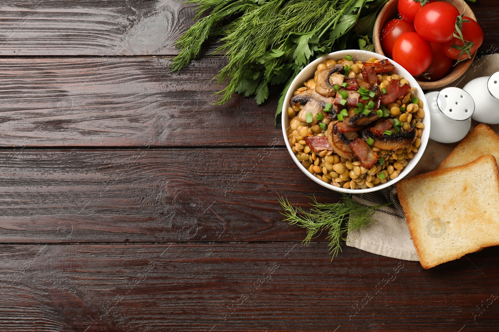 Photo of Delicious lentils with mushrooms, bacon and green onion in bowl served on wooden table, flat lay. Space for text