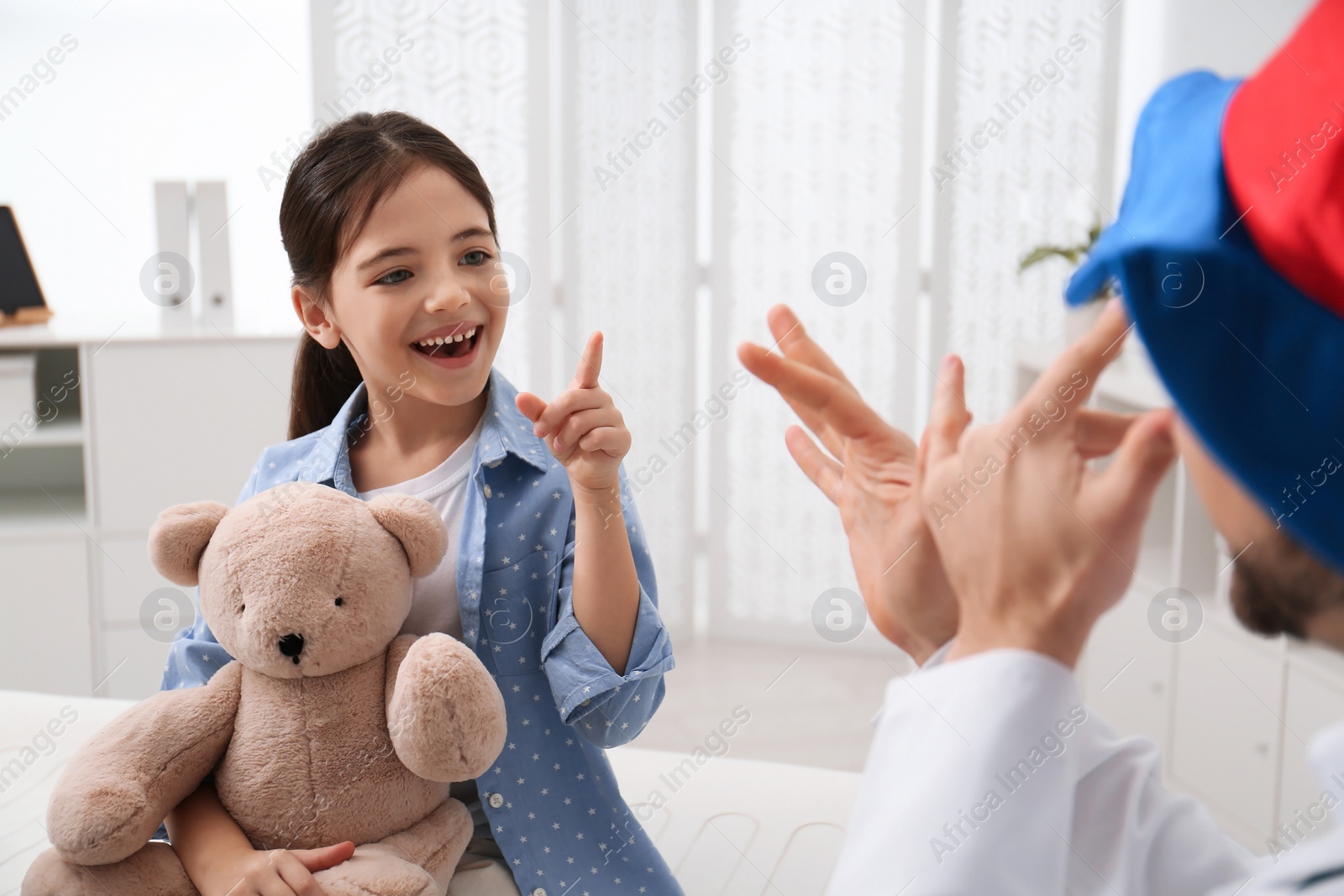 Photo of Pediatrician in funny hat playing with little girl during visit at hospital