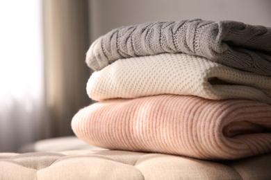 Photo of Stack of folded warm sweaters on couch indoors, closeup