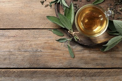 Cup of sage tea and green leaves on wooden table, top view. Space for text