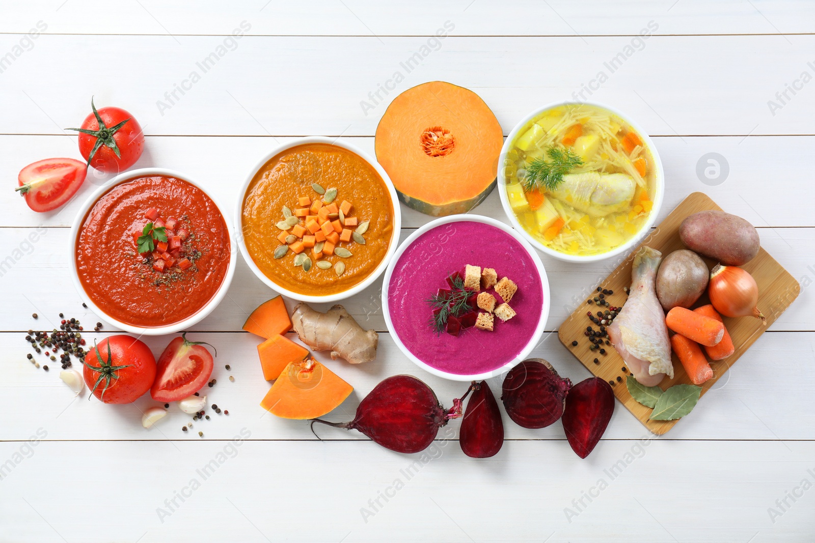 Photo of Tasty broth, different cream soups in bowls and ingredients on white wooden table, flat lay