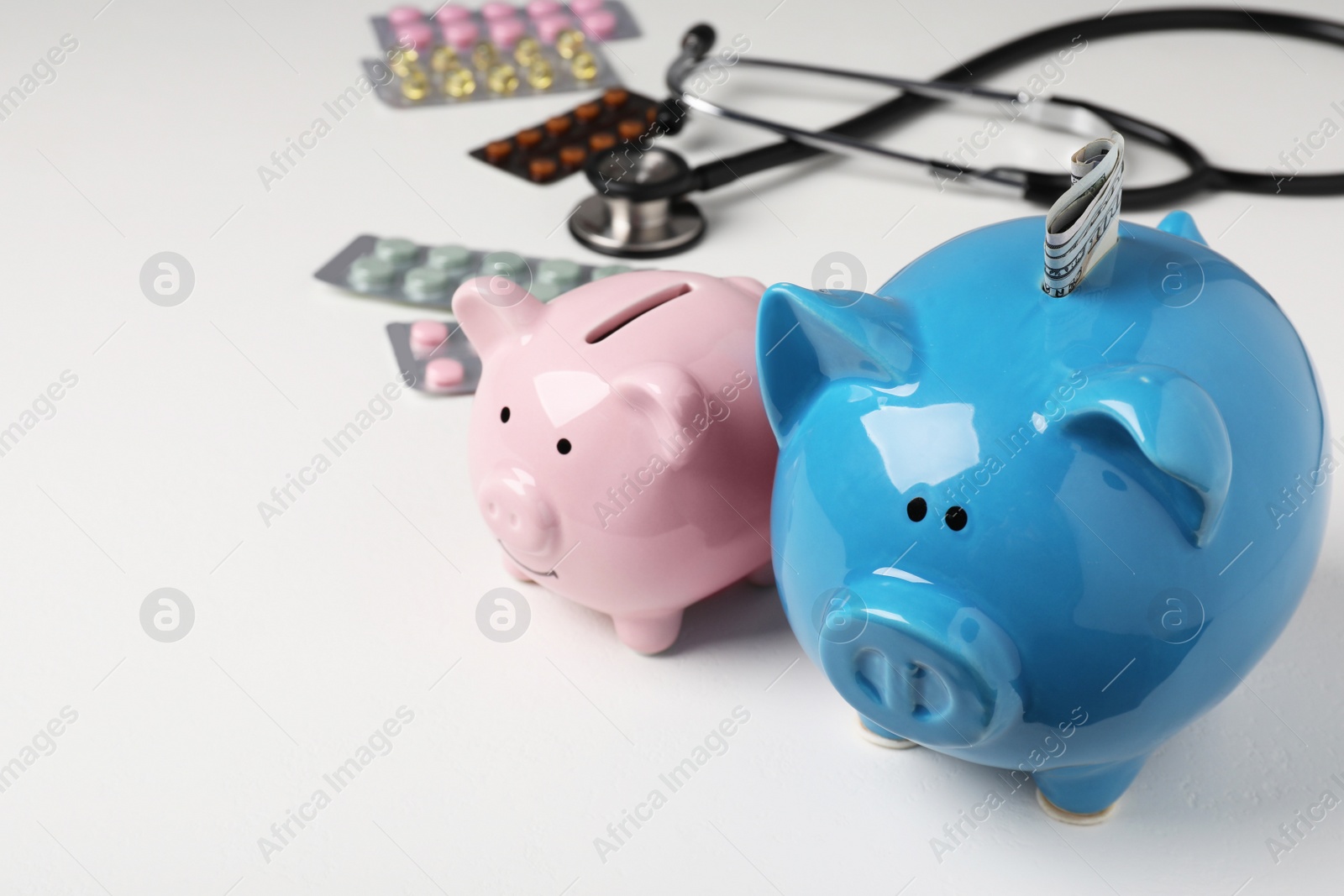 Photo of Piggy banks, stethoscope and pills on white textured table, closeup. Space for text. Medical insurance