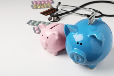 Photo of Piggy banks, stethoscope and pills on white textured table, closeup. Space for text. Medical insurance
