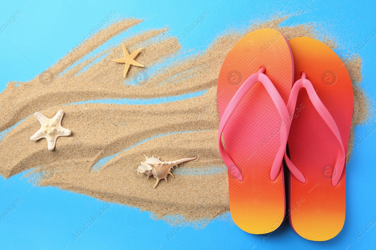 Photo of Flip flops and sand on light blue background, flat lay. Beach accessories