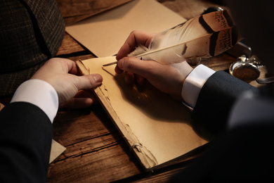 Photo of Detective writing with feather on paper at wooden table, closeup