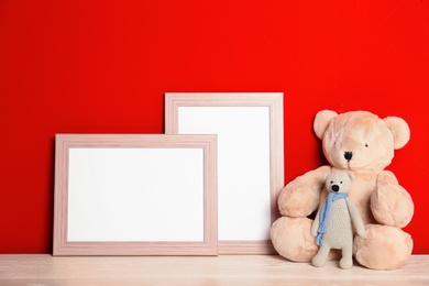 Photo of Soft toys and photo frames on table against red background, space for text. Child room interior