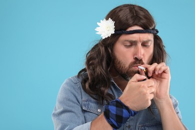 Photo of Stylish hippie man lighting cigarette on light blue background, space for text
