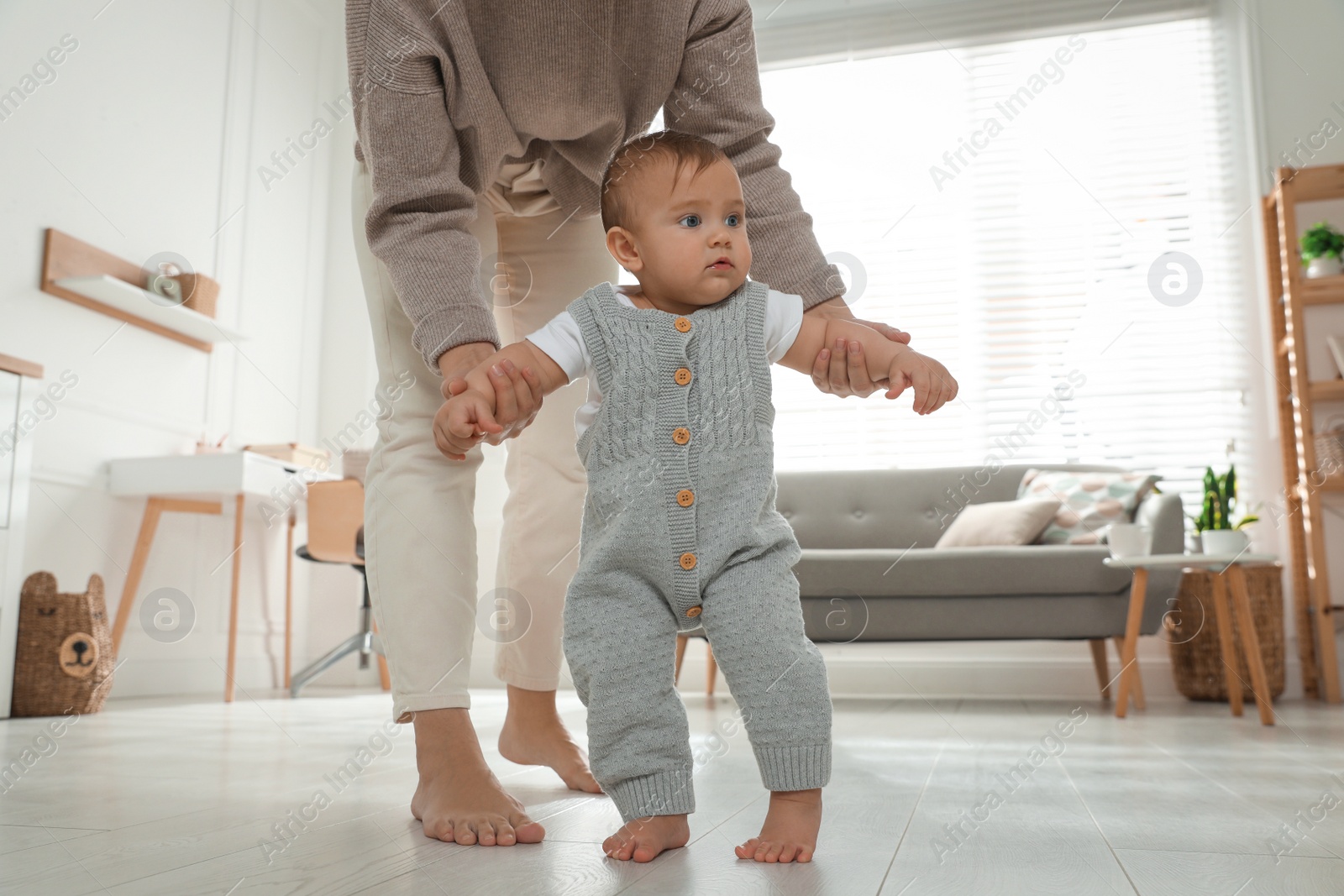 Photo of Mother supporting her baby daughter while she learning to walk at home