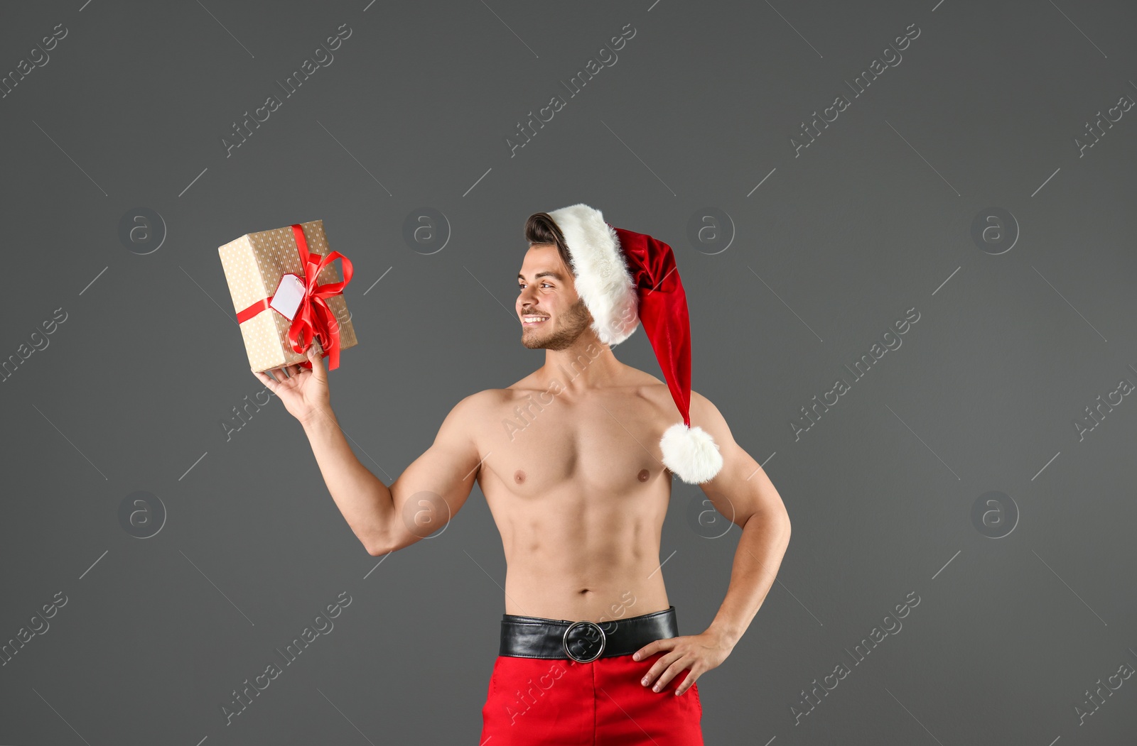 Photo of Shirtless sexy young Santa Claus with gift on color background