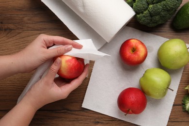 Photo of Woman wiping apple with paper towel at wooden table, top view