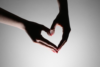 Woman making heart gesture on light background, closeup