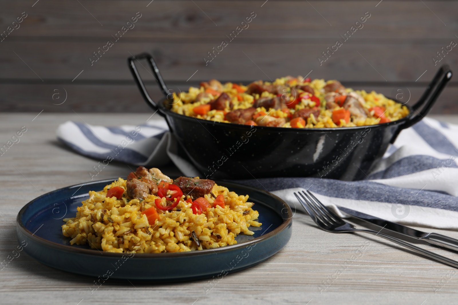 Photo of Delicious pilaf with meat, carrot and chili pepper on wooden table