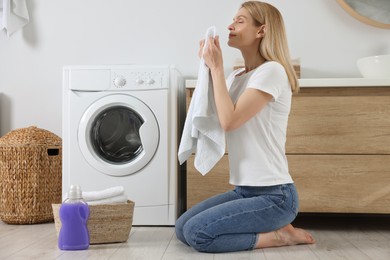 Photo of Woman smelling clean towels and sitting on floor near washing machine in bathroom, space for text