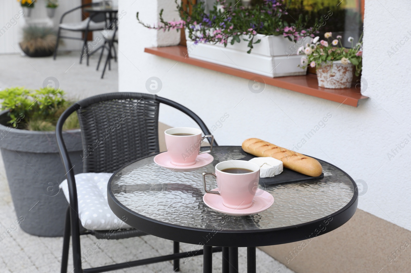 Photo of Cups of coffee, bread and cheese on glass table. Relaxing place at outdoor terrace