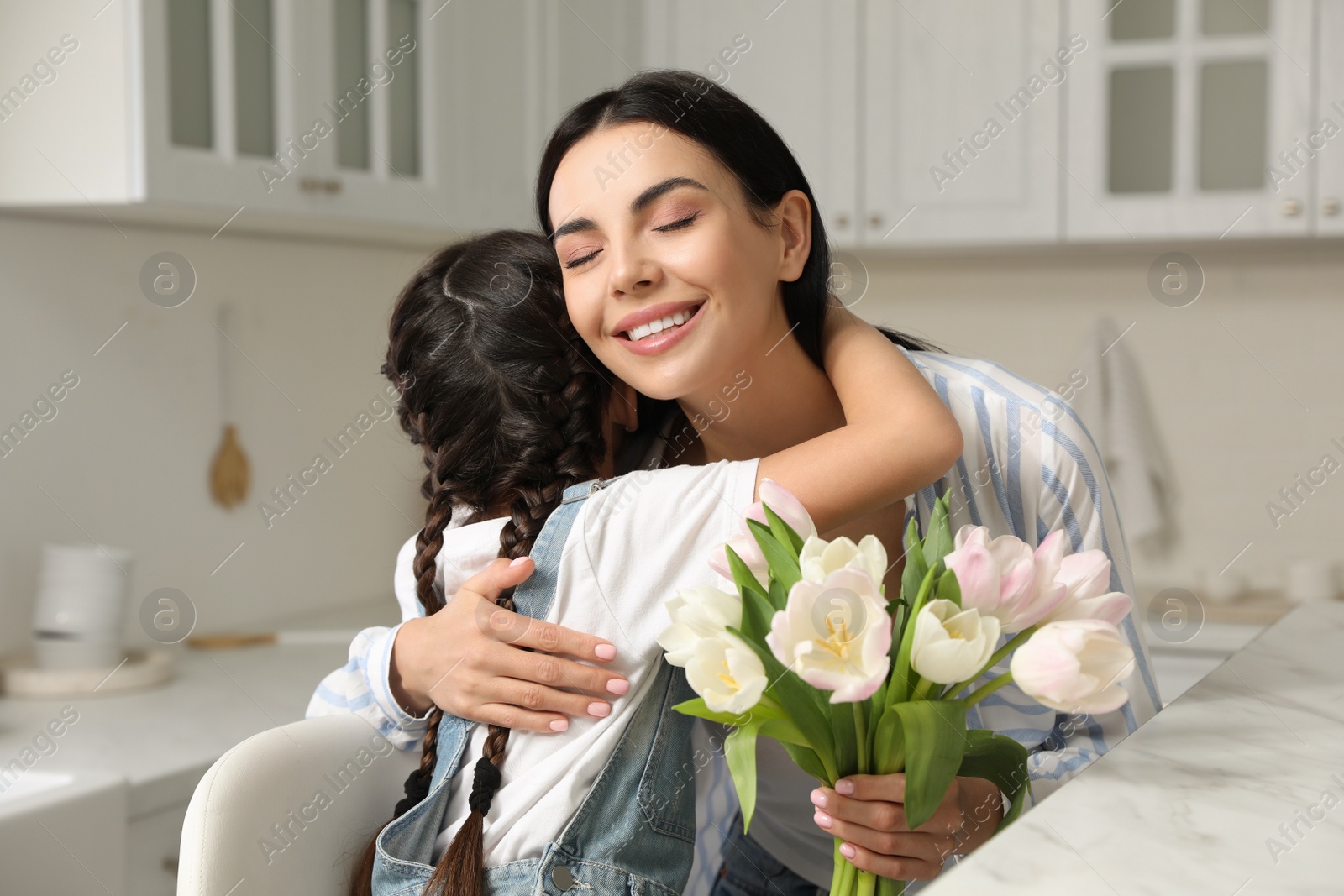 Photo of Little daughter congratulating her mom at table in kitchen. Happy Mother's Day