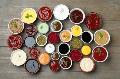 Photo of Many different sauces and herbs on wooden table, flat lay