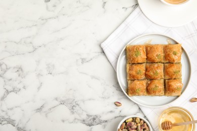 Delicious sweet baklava with pistachios and honey on white marble table, flat lay. Space for text