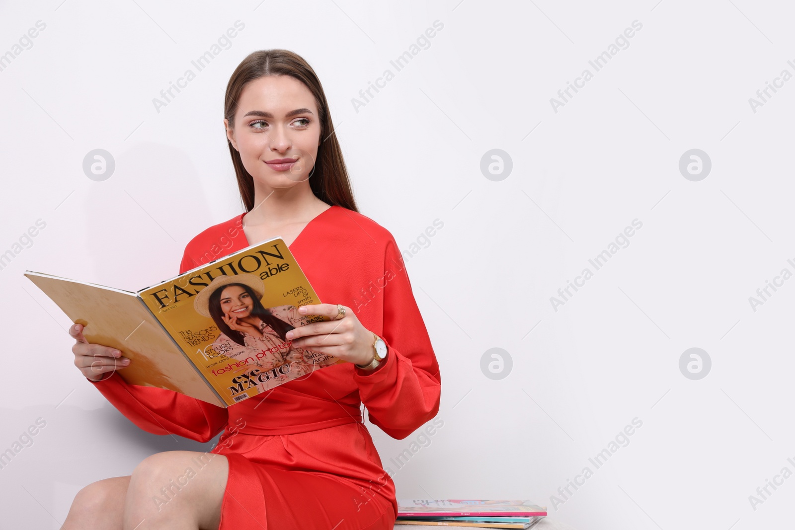 Photo of Young woman reading fashion magazine near white wall, space for text