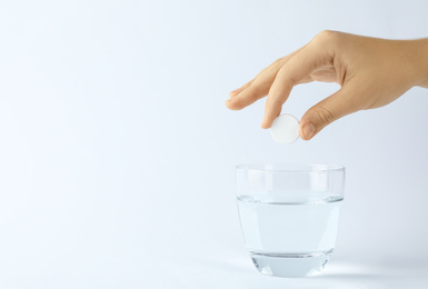 Photo of Woman putting tablet into glass of water on white background, space for text