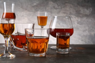Photo of Different delicious liqueurs in glasses on grey table