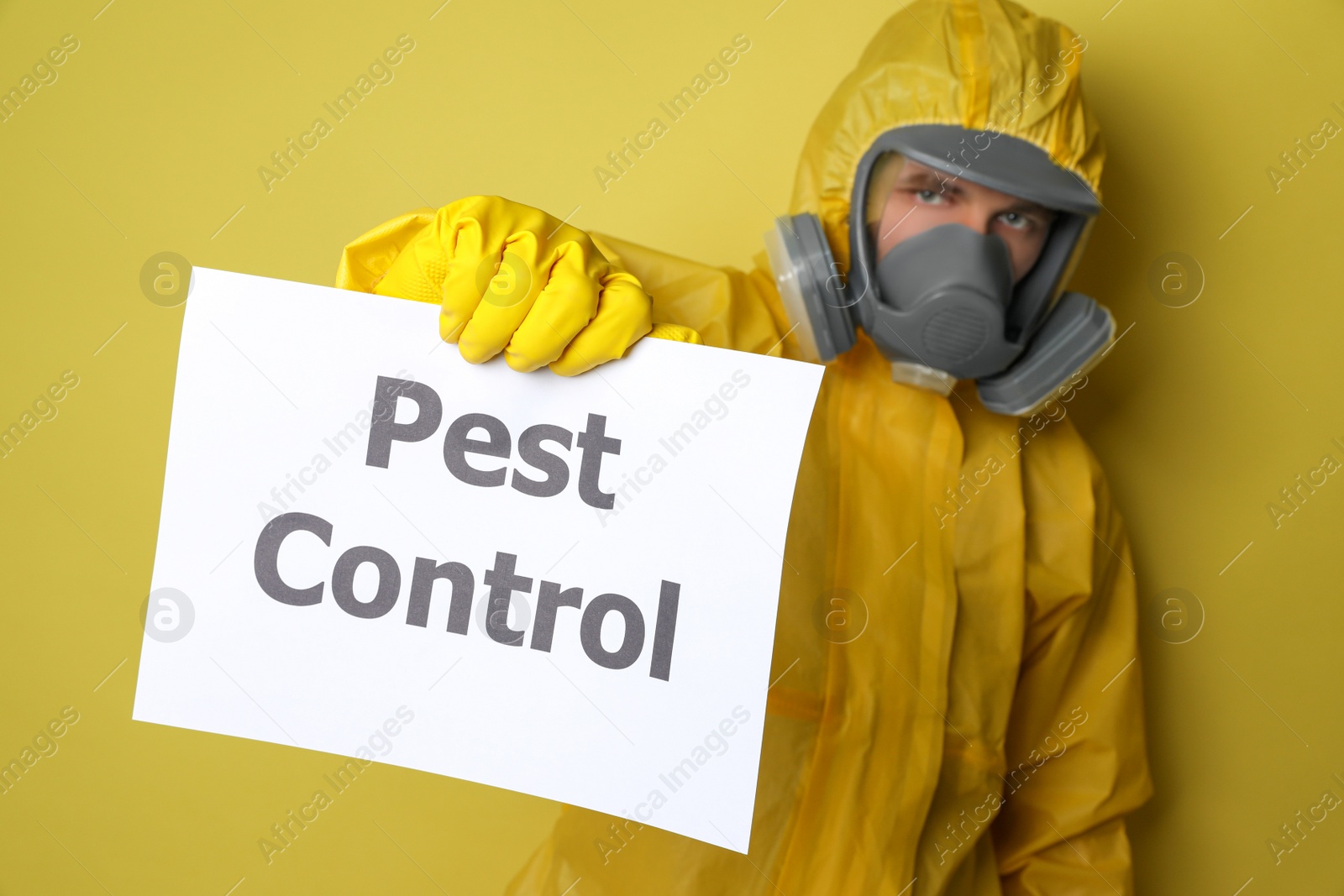 Photo of Man wearing protective suit with insecticide sprayer holding sign PEST CONTROL on yellow background