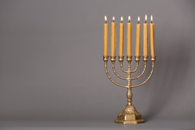 Golden menorah with burning candles on grey background, space for text