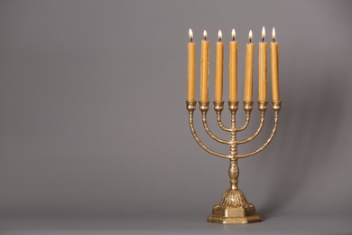 Photo of Golden menorah with burning candles on grey background, space for text