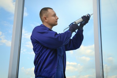 Construction worker sealing window with caulk indoors