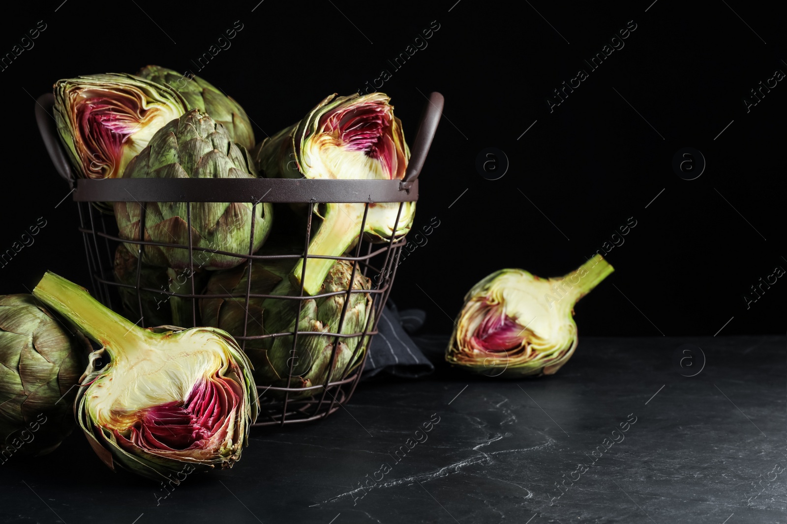 Photo of Cut and whole fresh raw artichokes on black table, space for text