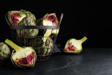 Photo of Cut and whole fresh raw artichokes on black table, space for text