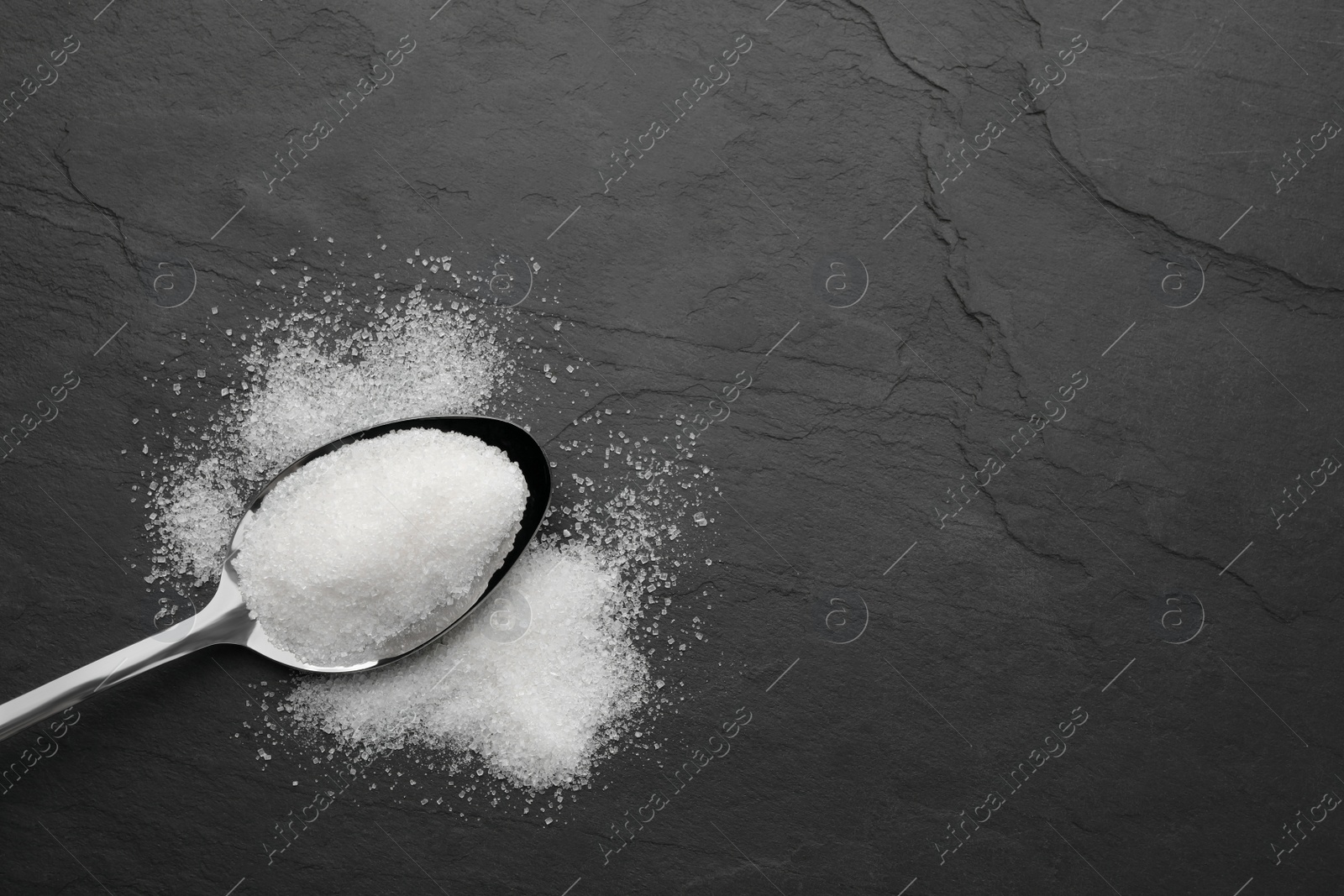 Photo of Granulated sugar and spoon on black table, top view. Space for text