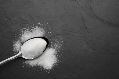 Granulated sugar and spoon on black table, top view. Space for text