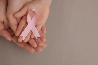 Photo of Family holding pink ribbon on grey background, top view with space for text. Breast cancer awareness